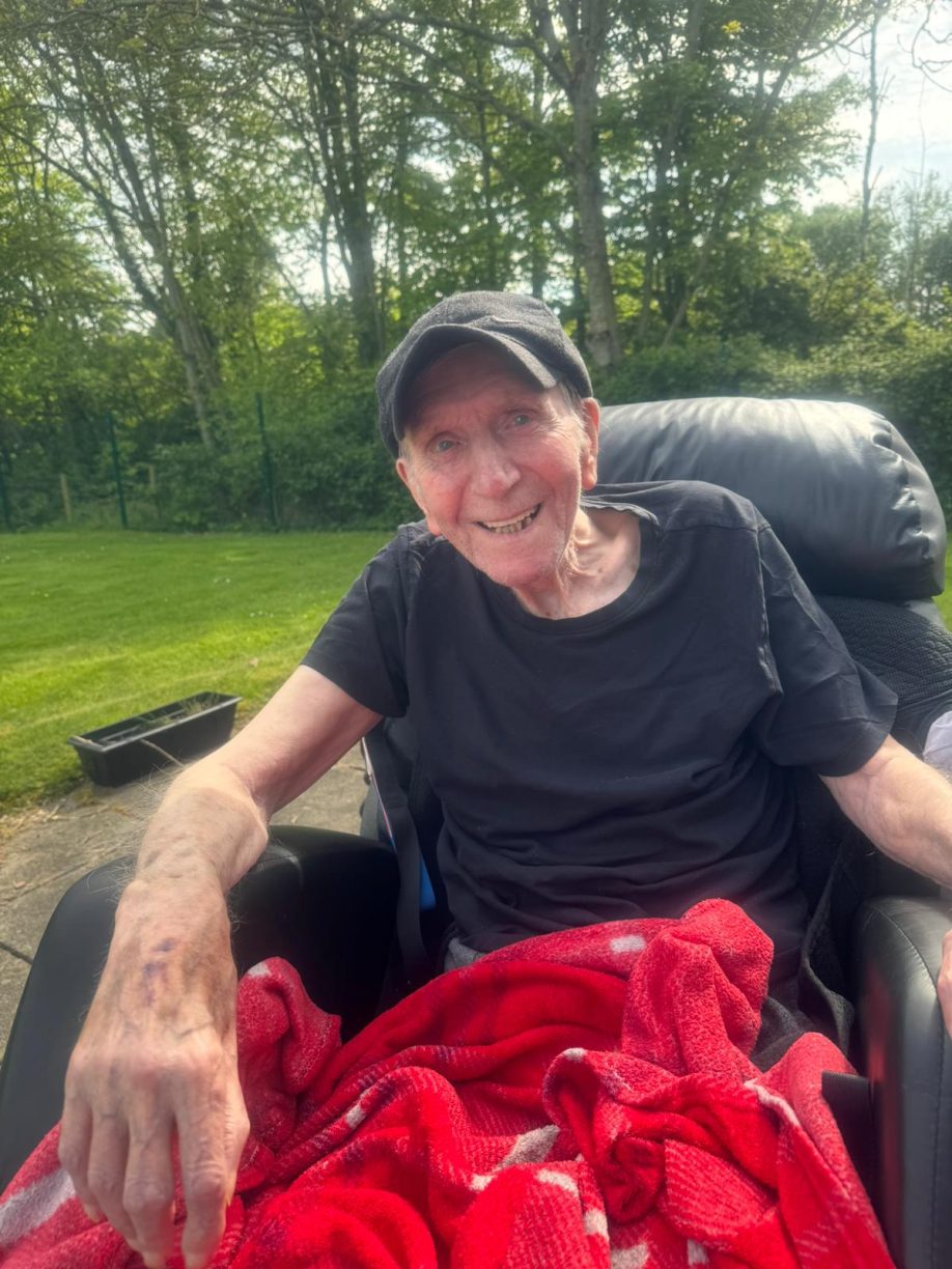 Barry enjoying the sunshine and accessible outdoor space at Fairways Newydd, promoting resident well-being and quality of life.