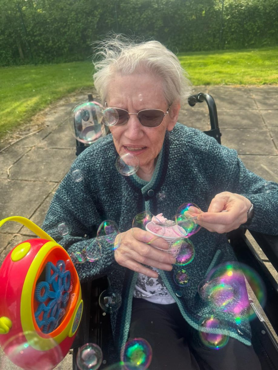 Pat enjoying outdoor activities and ice cream in the sunshine, promoting resident well-being and stimulating activities.