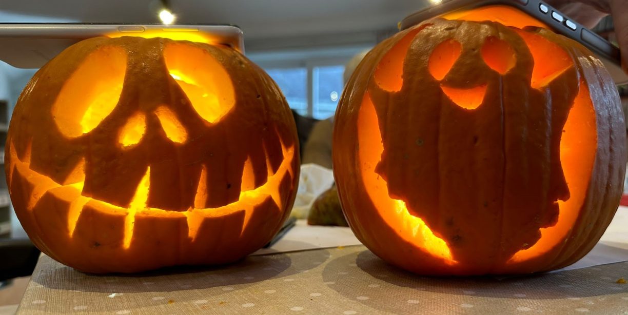 Two glowing jack-o'-lanterns on a table, one carved with a skull face and the other with a ghost.