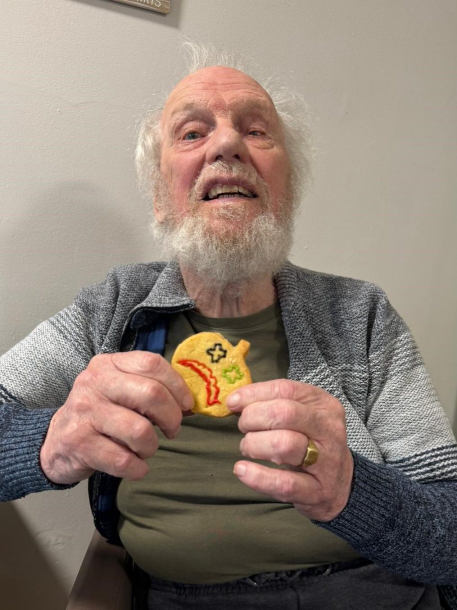 Elderly male resident smiling and holding a Halloween-decorated cookie.